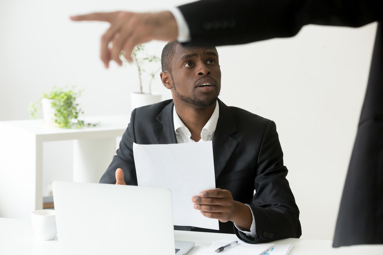 Employee holding a paper is given unfair discipline at work by an executive pointing towards the door.