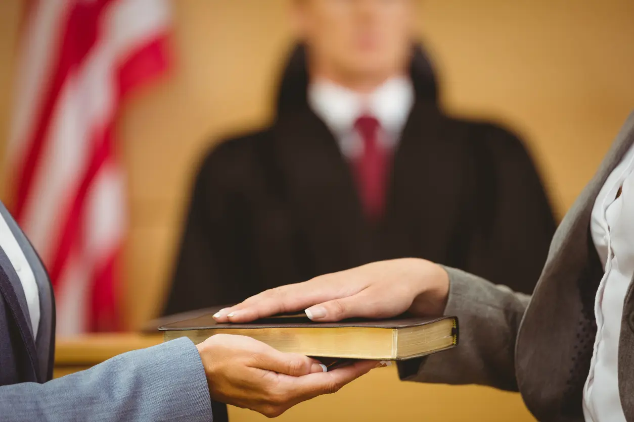 an expert witness swearing on a book in a courtroom in front of a judge.