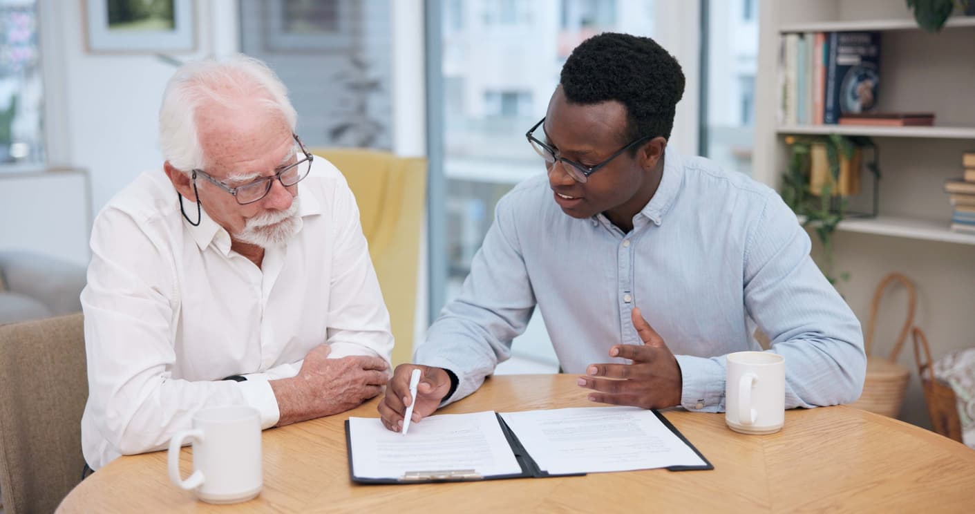 Insurance adjuster meeting with a client at the dinner table. The insurance adjuster is holding a marker and pointing out sections of a document to the client