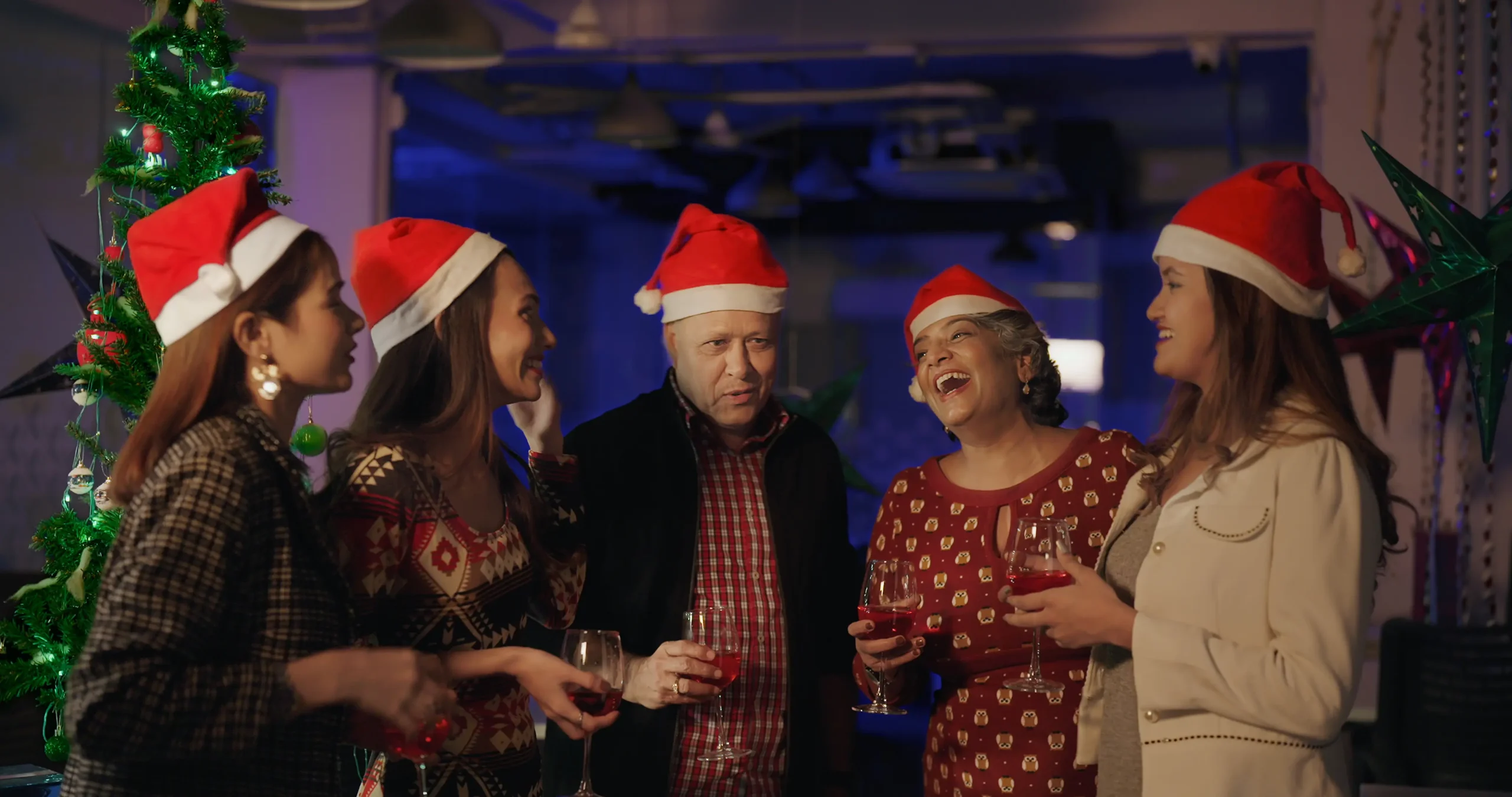 a company holiday party with employees gathered around in a semi-circle holding drinks, laughing, and having a good time