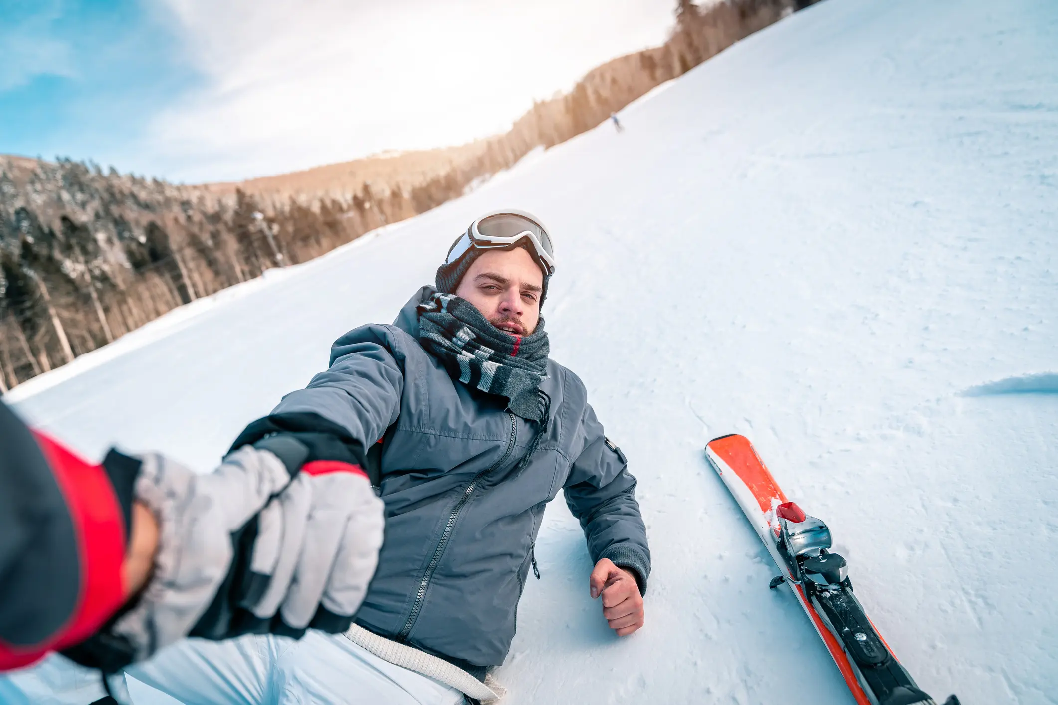 Skier in juried at a ski resort. Holding his knee as the arm of an emergency service worker extends out to him.