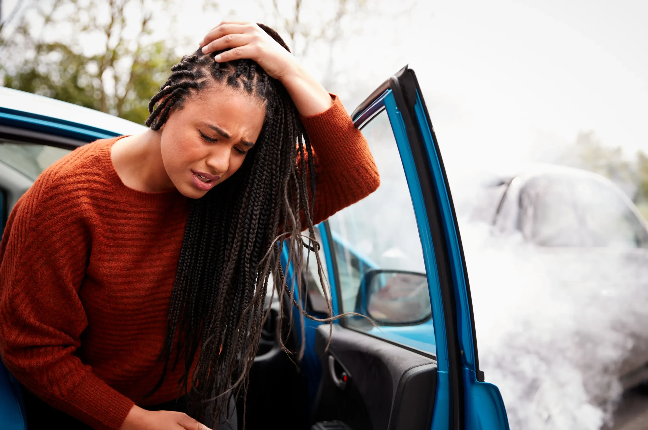 a woman exiting a car after an accident holding her head, experiencing traumatic brain injuries